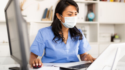 Arzthelferin mit Maske sitzt am Schreibtisch