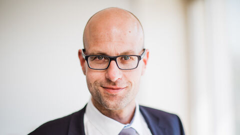 Markus Büttner lächelt frontal in die Kamera. Er trägt ein schwarzes Sakko, ein weißes Hemd und eine hell violette Krawatte.