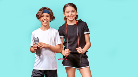 Zwei junge Teenager in Sportkleidung stehen vor einem türkisen Hintergrudn und lachen in die Kamera