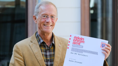 Staatsminister Wintermeyer hält den Förderbescheid für die SKV Büttelborn in den Händen und lächelt.