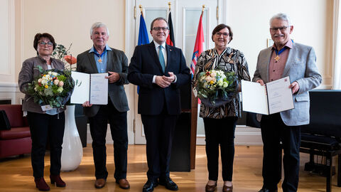 Die Geehrten stehen gemeinsam mit ihren Ehefrauen und Justizstaatssekretär Metz und ihren Auszeichnungen nebneinander und lächeln.