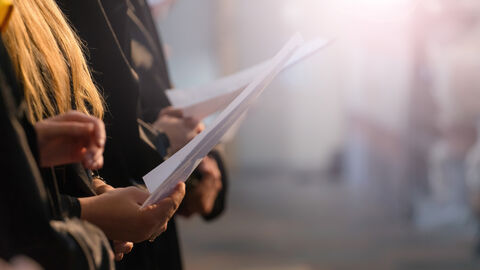 Singende Personen halten Papiere mit Liedtexten