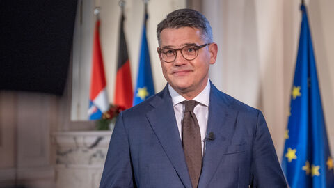 Ministerpräsident Boris Rhein steht vor Flaggen und schaut in die Kamera