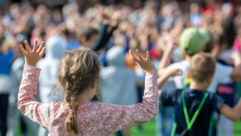 Ein Kind wird von hinten gezeigt, wie es die Arme gerade hoch hebt