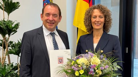 Finanzminister Lorz neben Konstanze Bepperling. Sie hält einen Blumenstrauß in Händen und er hält die Urkunde.