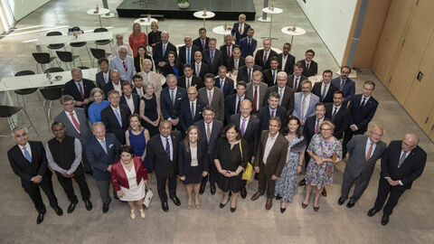 Männer und Frauen des hessischen Consular Corps stehen zusammen. Sie werden von oben fotografiert weswegen sie alle nach oben schauen und in die Kamera lächeln.