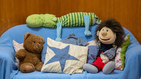 Kuscheltiere, Puppe und Kissen auf Sofa.