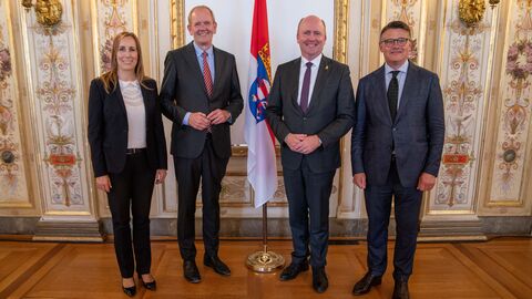 Vier Personen stehen zum Gruppenbild aufgestellt vor einer Wand und der Hessen-Flagge.