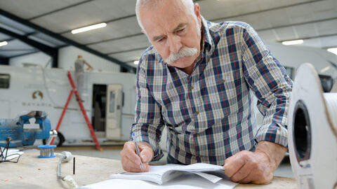 Mann im Rentenalter schaut konzentriert und schreibt etwas auf.
