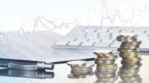 Auf dem Bild sind ein Stift, Münzen und Papier auf grauem Hintergrund zu sehen.