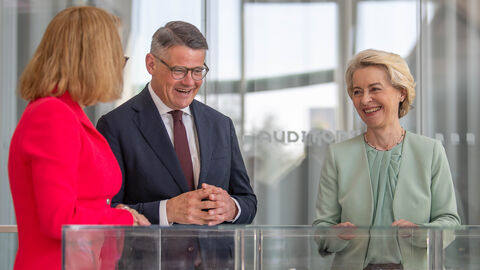 Ministerpräsident Rhein und Ursula von der Leyen stehen gemeinsam vor einem Kasten mit einem Modell. Sie unterhalten sich mit einer dritten Person.