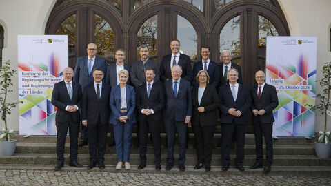 14 Männer und Frauen stehen in 2 Reihen vor einem Gebäude.