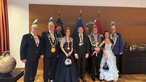 Minister Manfred Pentz steht mit dem Prinzenpaar sowie sechs weiteren festlich angezogenen Personen in einem Bürogebäude