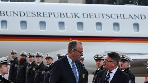 Zwei Männer stehen vor einem Flugzeug. Im Hintergrund stehen in zwei Reihen uniformierte Männer.